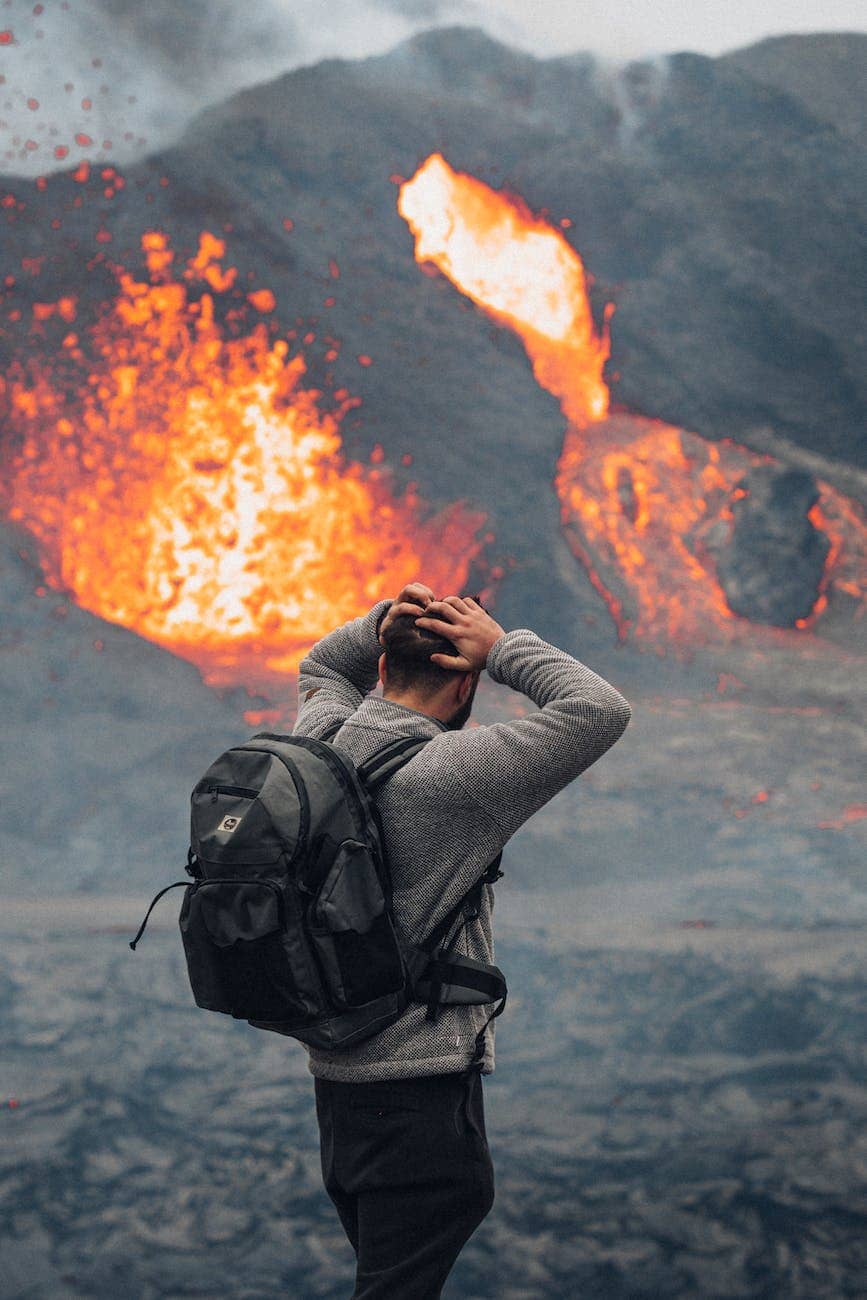 a man in gray jacket standing near the erupting volcano